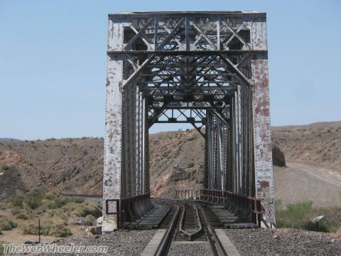 1996 Ford C-350 (Centurion Conversions) - A large, weathered metal railroad bridge spans a desert landscape under a clear blue sky.