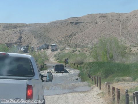 1996 Ford C-350 (Centurion Conversions) - Vehicles navigate a water crossing on a dirt road in a desert environment.
