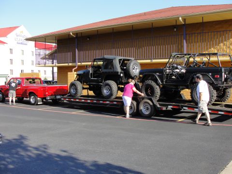 1967 Ford Mustang - Two off-road vehicles, a Jeep and a Bronco, are loaded onto a trailer towed by a red pickup truck.