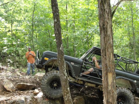 1967 Ford Mustang - A modified Ford Bronco navigates a challenging off-road course with a person standing nearby.