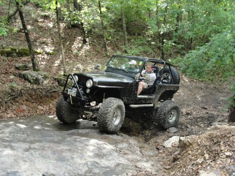 1967 Ford Mustang - Off-road Jeep CJ-7 tackling a challenging rocky path in a forest setting.