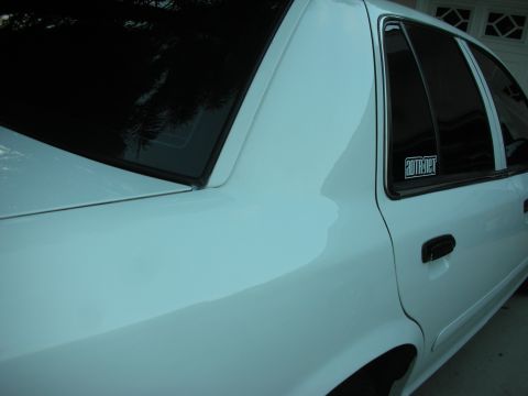 2004 Ford Crown Victoria - Side profile of a white 2004 Ford Crown Victoria, showing the rear quarter panel and tinted rear window with a sticker.