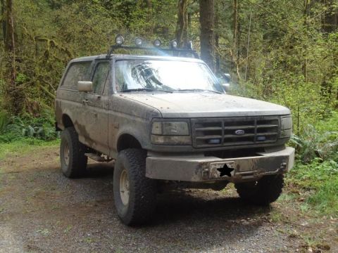 1995 Ford Bronco - Mud-covered 1995 Ford Bronco with roof-mounted lights and aftermarket bumper.