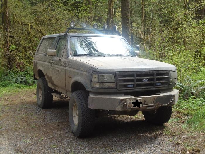 1995 Ford Bronco parked on a dirt road in a wooded area
