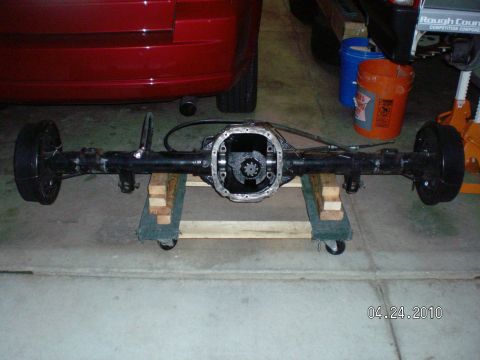 1996 Ford Bronco - A rear axle assembly is shown on a wooden stand with wheels, with a red vehicle in the background.
