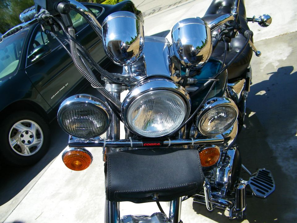 Motorcycle front end with chrome accents and a black pouch, parked next to a dark green car