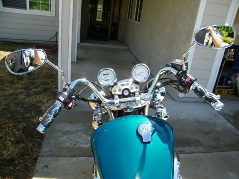 1992 Yamaha Virago - Close-up view of a teal motorcycle's handlebars and fuel tank, showing chrome accents and dual gauges.