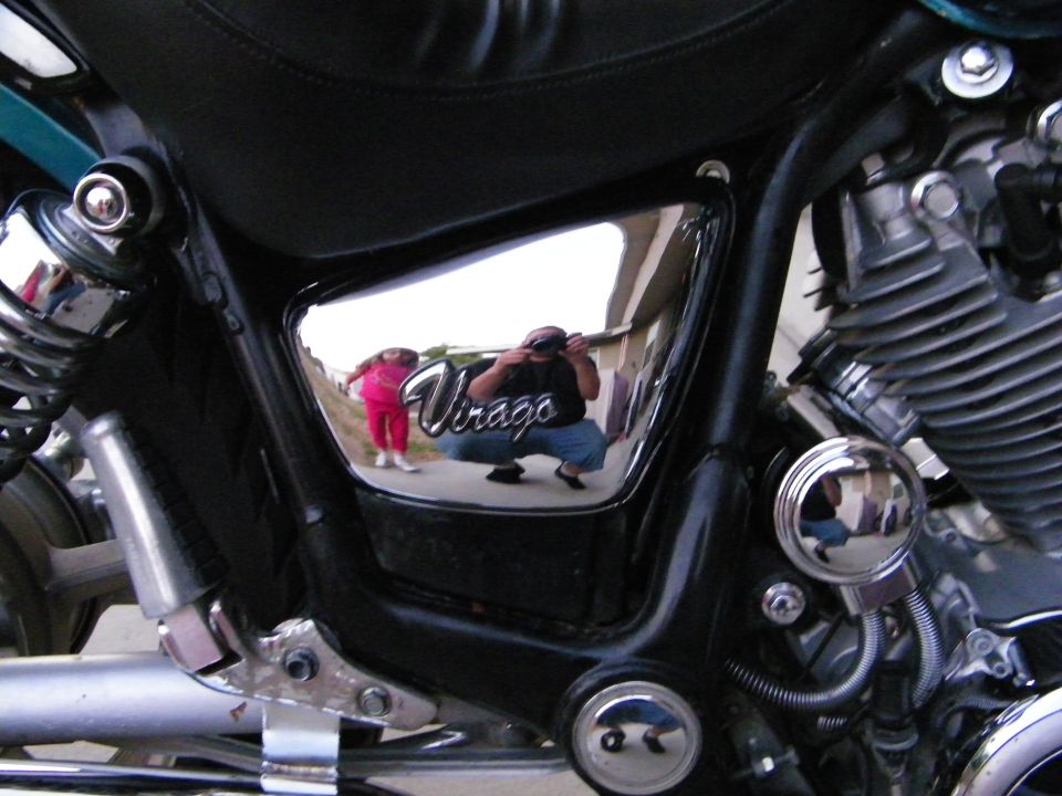 Reflection in chrome panel shows person taking photo and child in pink outfit