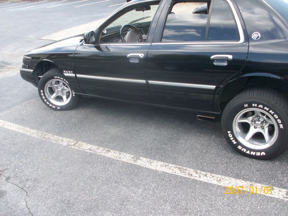 Black four-door sedan, passenger side, with white-letter Hankook tires and chrome wheels