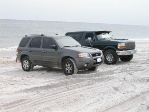 1994 Ford Bronco - Two SUVs are parked on a sandy beach with the ocean in the background.