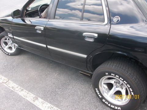1993 Mercury Grand Marquis - A black sedan with chrome accents and custom wheels is parked on asphalt.