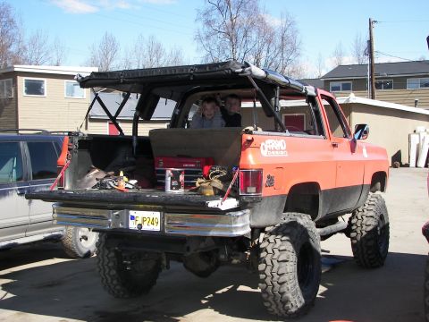1990 Chevrolet Suburban - This lifted SUV has a soft top and a toolbox in the bed, with two children visible in the rear seats.