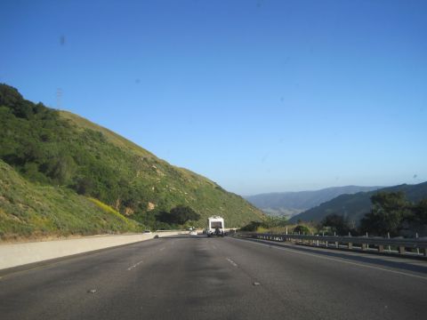 1989 Toyota Pickup/SR5 - A view from a vehicle driving on a highway with a large green hill to the left and mountains in the distance.
