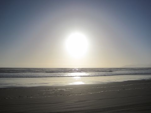 1989 Toyota Pickup/SR5 - Ocean waves crash on a sandy beach under a bright, hazy sun.