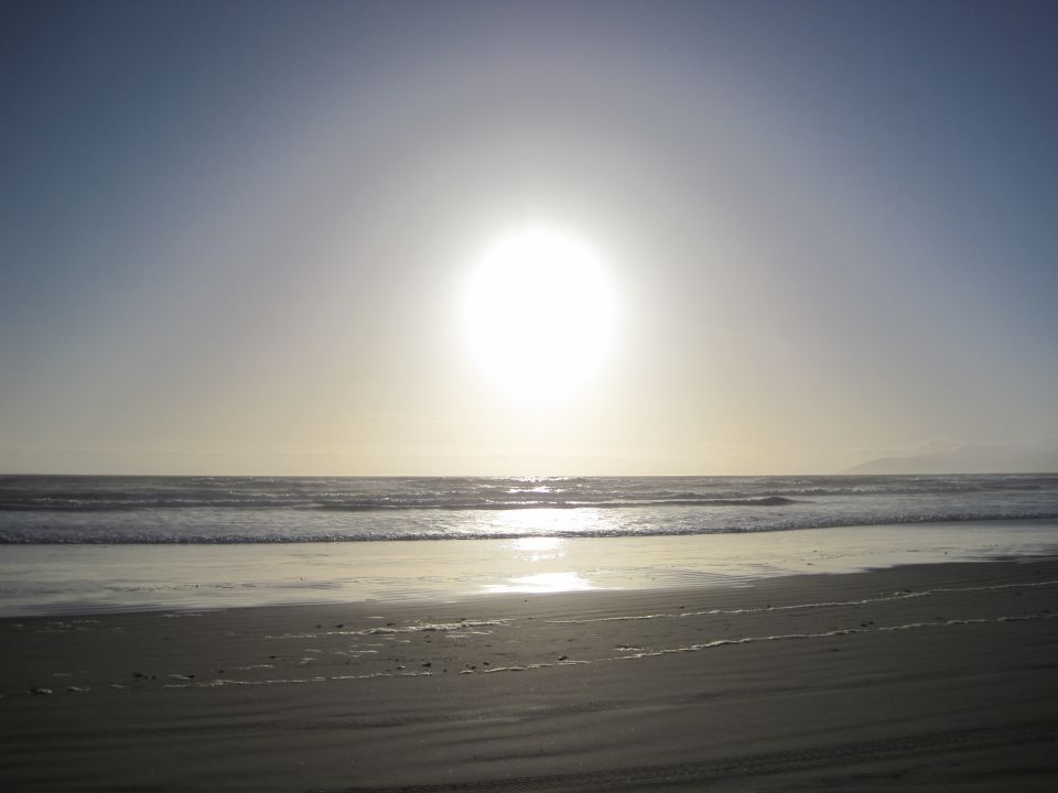 Beach with waves and a bright sun low in the sky