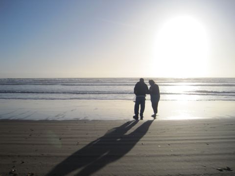 1989 Toyota Pickup/SR5 - Two figures cast long shadows on the sand as they walk along the shore under a bright, hazy sun.