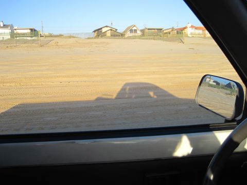 1989 Toyota Pickup/SR5 - View from inside a vehicle shows the shadow of a pickup truck on a sandy beach, with houses visible in the distance.