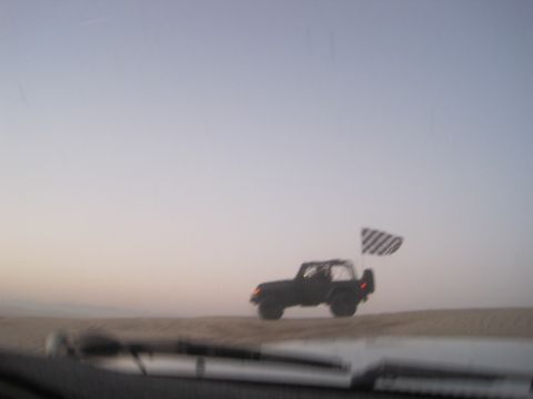 1989 Toyota Pickup/SR5 - A Jeep Wrangler with a checkered flag flies across a sandy dune at sunset.