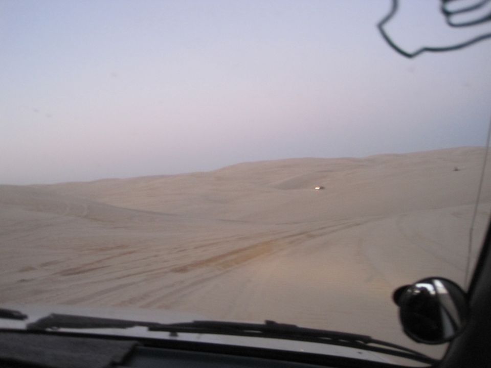 view from inside a vehicle driving through sand dunes, with another vehicle visible in the distance