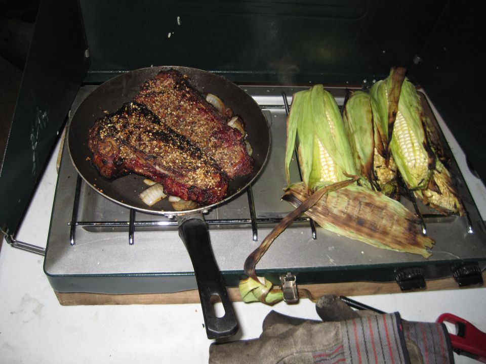 Camping stove with steak in a pan and corn on the cob