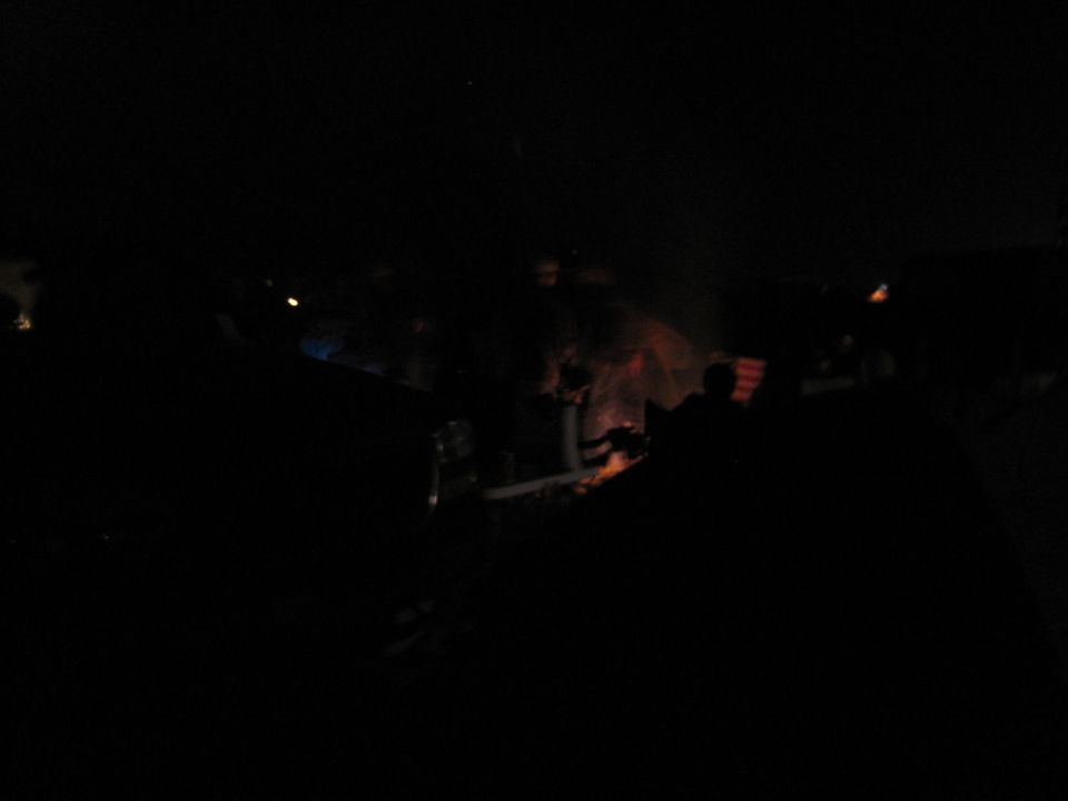 Dark scene with multiple vehicles and a campfire
