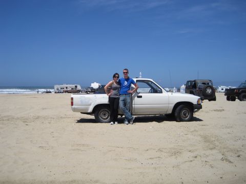 1989 Toyota Pickup/SR5 - A couple poses in front of a white pickup truck on a beach with other vehicles and RVs in the distance.
