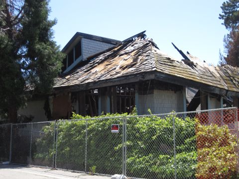 1989 Toyota Pickup/SR5 - A house with severe roof damage is cordoned off by a fence.