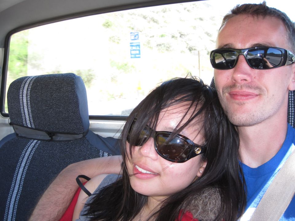 Two people wearing sunglasses inside a vehicle, looking at the camera