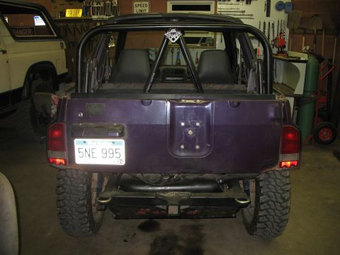 1985 Ford Bronco - Purple SUV with roll cage and aftermarket tires parked next to a white Ford Bronco in a garage.