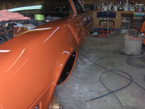 1980 Chevrolet Camaro - Close-up of an orange 1980 Chevrolet Camaro's fender and wheel well in a garage setting.