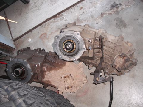 1991 Ford Bronco - Two automotive transfer cases are shown on a concrete floor, one a silver flange.