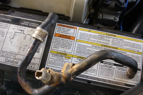 1995 Ford Taurus - Close-up of engine hoses and various warning labels, including information on coolant and air conditioning systems.