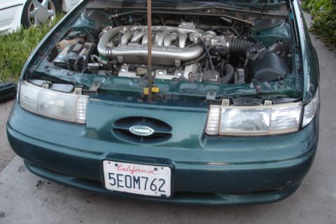 1993 Ford Taurus - The front of a green 1992 Ford Taurus is visible, with the hood open to reveal the engine compartment and a Yamaha emblem on the grille.