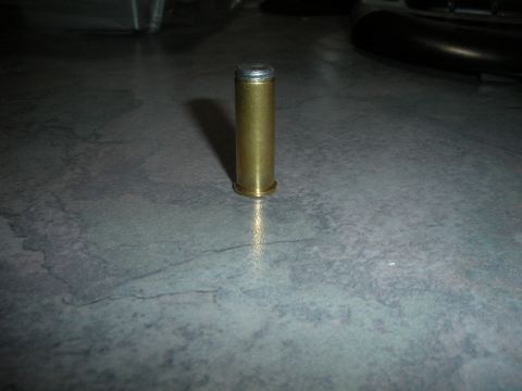 1996 Ford Bronco - A single brass ammunition cartridge is shown standing upright on a speckled surface, with a portion of a vehicle visible in the background.