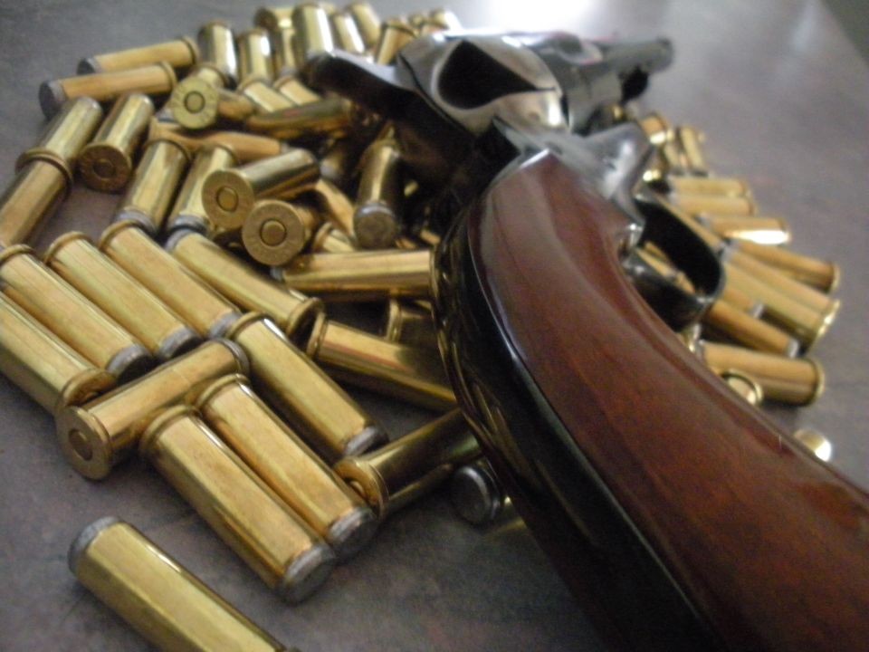 Revolver with wooden grip and pile of brass cartridges on a metallic surface