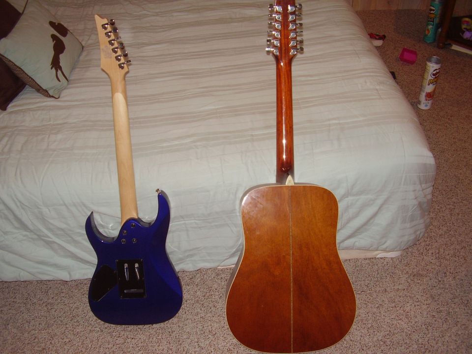 blue electric guitar and a brown acoustic 12-string guitar on a bed