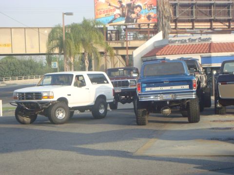 1986 Ford Bronco - A white Ford Bronco is parked next to other trucks, with a billboard in the background.