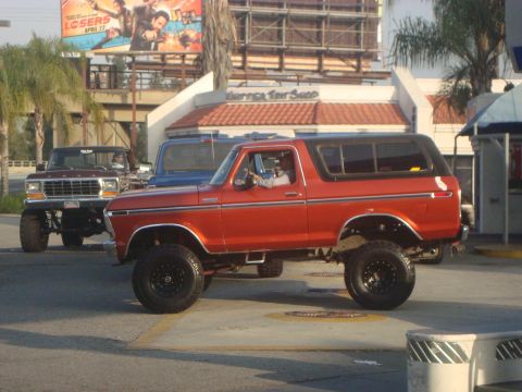 1986 Ford Bronco - This lifted orange Ford Bronco is seen driving alongside other trucks.