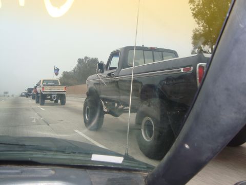 1986 Ford Bronco - Multiple lifted pickup trucks are seen on the highway in foggy conditions.