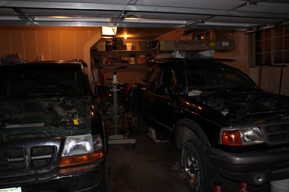 Two pickup trucks, one green and one black, parked in a garage with hoods open