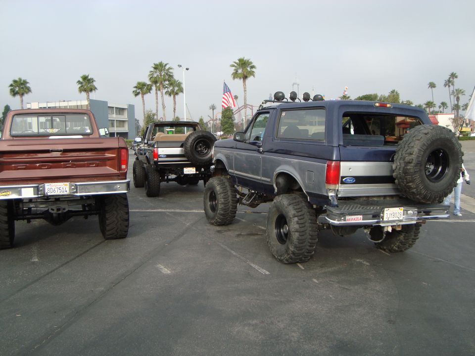 Blue Ford Bronco with spare tire on back, parked next to two trucks