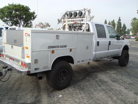 1986 Ford Bronco - This silver pickup truck features a utility bed and off-road tires, with 'CERVANTES RACING' visible on its side.