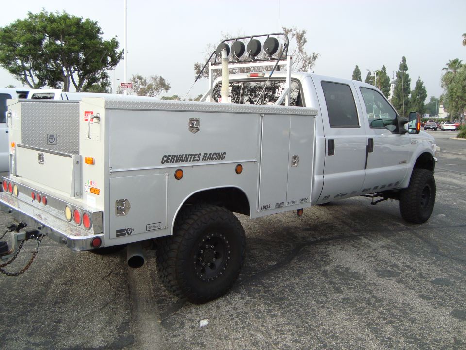 Silver pickup truck with utility bed, off-road tires, and light bar on roof. Text 'CERVANTES RACING' visible on the side