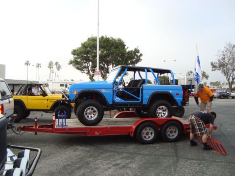 1986 Ford Bronco - Two Ford Broncos are parked outside, one blue and one yellow, with people around them.