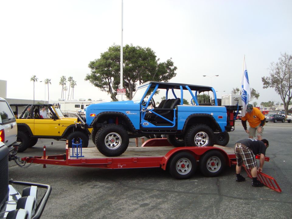 Blue Ford Bronco with roll cage on a trailer, yellow Ford Bronco behind it