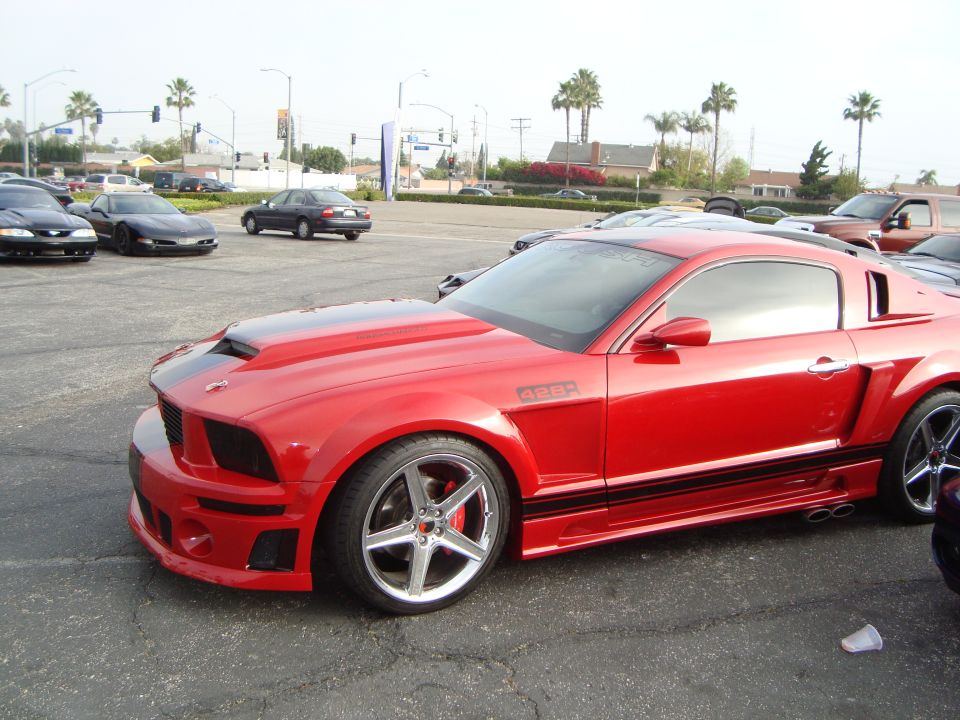 Red Ford Mustang with a hood scoop and black racing stripes, parked on asphalt