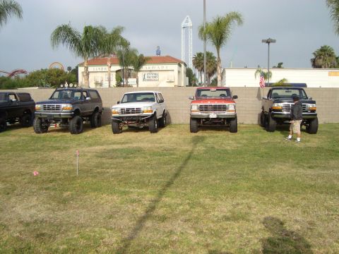 1986 Ford Bronco - A lineup of lifted Ford trucks and SUVs, including a 1992 Bronco, parked on a grassy field.