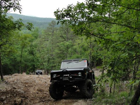 1967 Ford Mustang - Off-road vehicles navigate a challenging rocky trail surrounded by dense forest.
