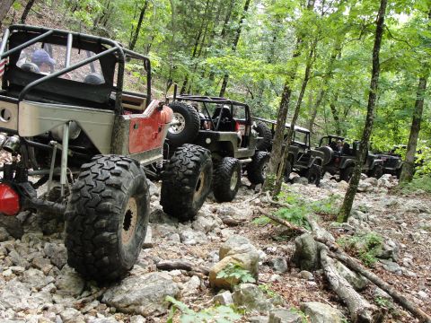 1967 Ford Mustang - Multiple modified Jeeps navigate a challenging, rocky trail through a wooded area.