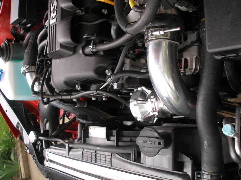 Polished intercooler charge pipe and BOV flange over a coolant tank in a red engine bay